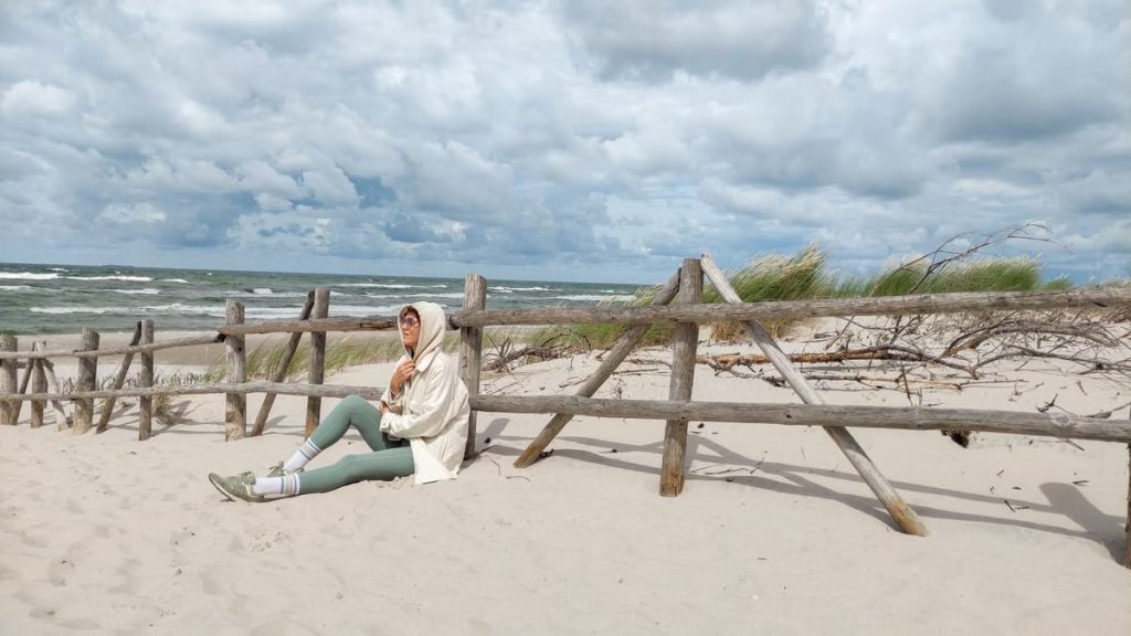 Person in casual attire sits on Baltic beach, enjoying the serene sea view.