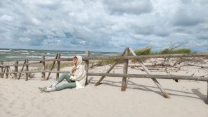 Person in casual attire sits on Baltic beach, enjoying the serene sea view.